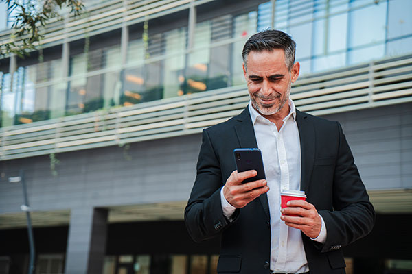 Seasoned Businessman in Action: portrait of a mature professional checks his mobile phone while enjoying a coffee outside the office, capturing a moment of balance between work and relaxation.